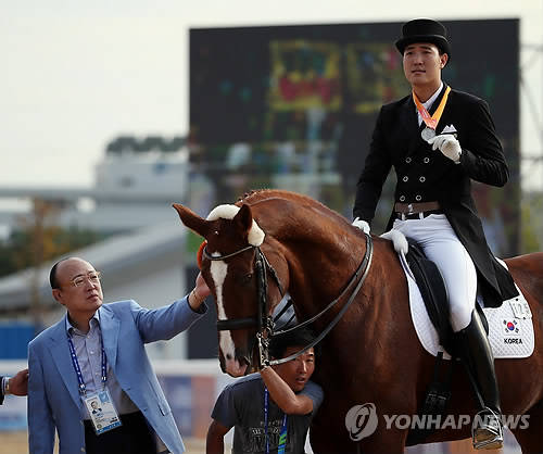 지난달 23일 인천 드림파크 승마장에서 한화그룹 김승연 회장(왼쪽)이 2014 인천 아시안게임 승마 마장마술 개인전에서 은메달을 획득한 아들 김동선의 말을 쓰다듬고 있다(사진: 연합뉴스)