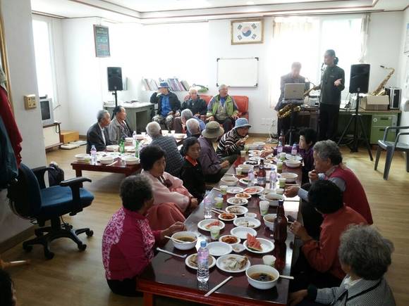▲( 어르신들께서 색소폰 연주와 작은 음악회를 즐기며 점심 식사를 하고 있다.)