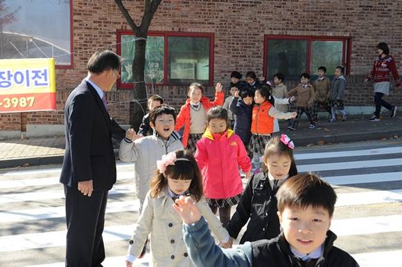 인터뷰를 마친 김진우 의장이 횡단보도를 건너고 있는 아이들에게 서스럼없이 다가가 웃으며 아이들이 안전하게 건널수 있도록 안내 하고 있다.(사진=수원시의회 제공)