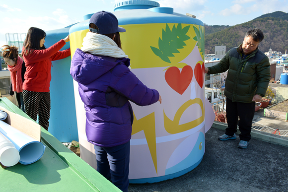 영산대 LINC사업단 도시활력디자인 탐사단 중 ‘마을 미술프로젝트를 통한 반송 도시 색채 계획’팀이 보기 흉한 옥상 물탱크에 다양한 테마를 주제로 디자인한 시트지를 덧붙이는 색채디자인 작업을 하고 있다. (사진제공=영산대)