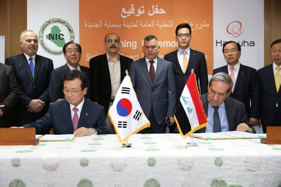 한화건설 이근포 대표이사(태극기 좌측)와 사미 알 아라지 이라크 NIC 의장(이라크 국기 우측)이 한화건설 관계자와 이라크 정부인사들이 지켜보고 있는 가운데, 한화건설의 21.2억달러 규모 이라크 비스마야 신도시 사회기반시설공사 수주를 위한 서명하고 있다.(사진 제공: 한화건설)
