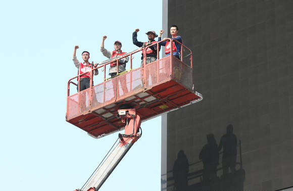 서울 소공동 서울중앙우체국 옆 광고탑에서 80일간 고공농성을 벌인 장연의 SK브로드밴드 비정규직지부 연대팀장(왼쪽 두번째)과 강세웅 LG유플러스 비정규직지부 조직부장(왼쪽 세번째)이 26일 오후 고공농성을 종료한 뒤 크레인을 타고 광고탑에서 내려오고 있다(사진: 연합뉴스)